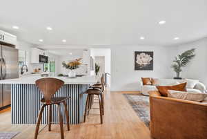 Kitchen with white cabinetry, recessed lighting, light wood-type flooring, a kitchen bar, and freestanding refrigerator