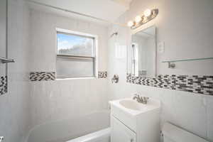 Full bath featuring shower / tub combination, vanity, and tile walls