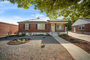View of front of home with xeriscaped yard, roof mounted solar panels, brick siding, roof with shingles, and a porch