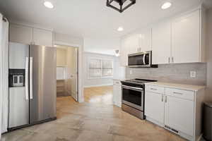 Kitchen with appliances with stainless steel finishes, white cabinets, tasteful backsplash, tile floors, and recessed lighting