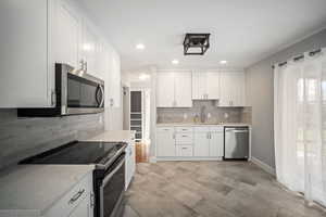 Kitchen with appliances with stainless steel finishes, backsplash, white cabinets, light stone counters, tile floors, and recessed lighting
