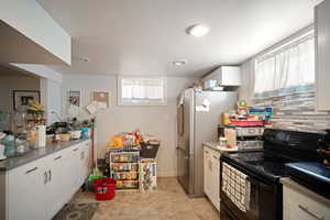 Kitchen featuring black electric range oven, white cabinetry, freestanding refrigerator, tasteful backsplash, and recessed lighting