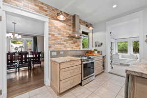 Kitchen with stainless steel gas stove, granite countertops, wall chimney exhaust hood, and plenty of natural light