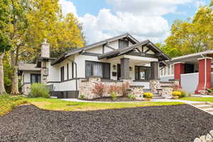 View of front of property with stucco basement entrance, front porch, a chimney, and stone siding