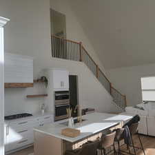 Kitchen featuring light wood-type flooring, white cabinets, a breakfast bar area, light stone counters, and high vaulted ceiling