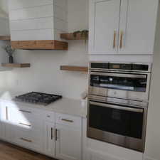 Kitchen featuring open shelves, appliances with stainless steel finishes, white cabinetry, and custom range hood