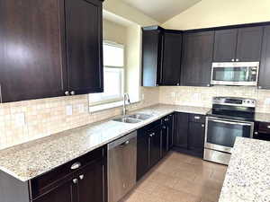 Kitchen featuring stainless steel appliances, light stone countertops, tasteful backsplash, vaulted ceiling, and light tile patterned floors
