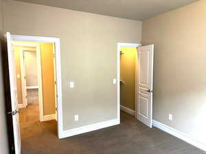 Unfurnished bedroom featuring dark colored carpet and baseboards