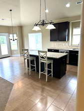 Kitchen featuring a textured ceiling, tasteful backsplash, a kitchen bar, pendant lighting, and light tile patterned floors