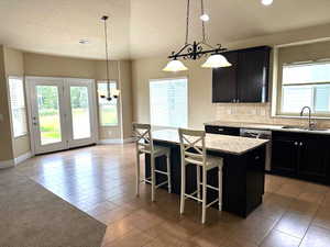 Kitchen with dark cabinetry, pendant lighting, a textured ceiling, light tile patterned floors, and a center island