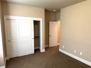 Unfurnished bedroom with dark colored carpet, a closet, and a textured ceiling
