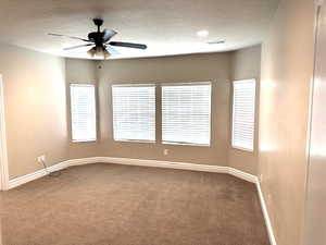 Carpeted empty room featuring a textured ceiling and ceiling fan
