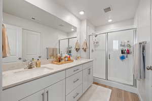Bathroom featuring double vanity, a stall shower, and light wood-style flooring