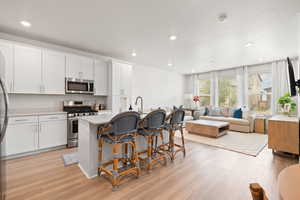 Kitchen with a breakfast bar area, a kitchen island with sink, appliances with stainless steel finishes, light wood-style floors, and white cabinets