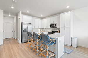 Kitchen featuring stainless steel appliances, white cabinets, a center island with sink, light stone counters, and light wood-style flooring