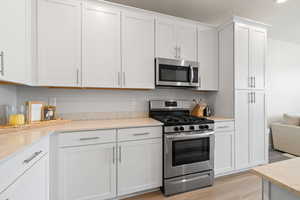 Kitchen featuring stainless steel appliances, light wood-style flooring, white cabinetry, and light stone counters