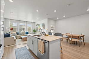 Kitchen with light stone countertops, stainless steel dishwasher, a kitchen island with sink, light wood finished floors, and recessed lighting