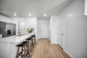 Kitchen with a breakfast bar area, a peninsula, light wood-style flooring, stainless steel fridge with ice dispenser, and light stone counters