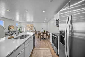 Kitchen featuring stainless steel appliances, white cabinets, light wood-style floors, open floor plan, and recessed lighting