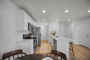 Kitchen with a peninsula, stainless steel appliances, a kitchen breakfast bar, white cabinets, and light wood-type flooring
