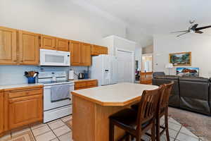 Kitchen with light countertops, white appliances, open floor plan, a breakfast bar, and high vaulted ceiling