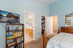 Bedroom with light carpet, a walk in closet, light tile patterned flooring, connected bathroom, and a high ceiling