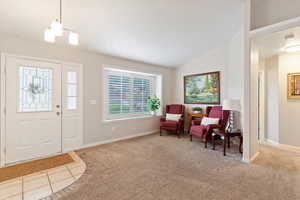 Carpeted foyer entrance with lofted ceiling, tile patterned flooring, and a chandelier
