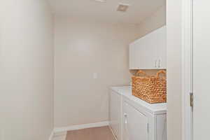 Laundry area featuring cabinet space, light tile patterned flooring, and independent washer and dryer
