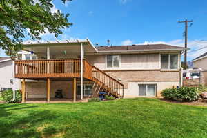 Back of property with brick siding, stairway, a wooden deck, a patio area, and a yard