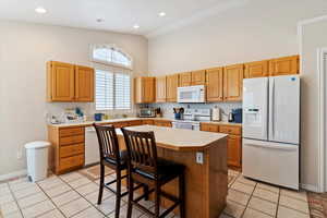 Kitchen featuring white appliances, light countertops, a kitchen breakfast bar, light tile patterned flooring, and a towering ceiling