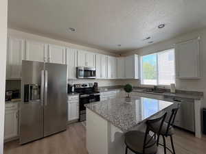 Kitchen featuring appliances with stainless steel finishes, light wood-type flooring, white cabinets, a kitchen breakfast bar, and a center island