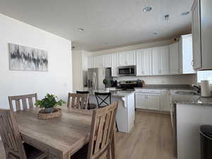Kitchen with light stone countertops, light wood-style flooring, appliances with stainless steel finishes, a textured ceiling, and white cabinets