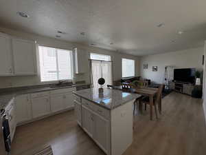 Kitchen featuring white cabinetry, light stone countertops, light wood-type flooring, a kitchen island, and a textured ceiling