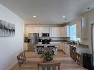 Kitchen featuring stainless steel appliances, white cabinets, a kitchen island, light wood-style flooring, and recessed lighting