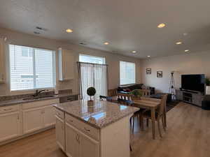 Kitchen with light wood-type flooring, light stone counters, a kitchen island, open floor plan, and recessed lighting