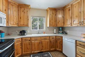Kitchen featuring white appliances, light countertops, dark tile patterned flooring, and brown cabinets