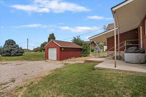View of grassy yard with a garage, driveway, and an outbuilding