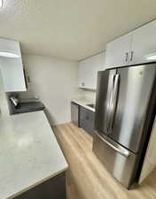 Kitchen featuring white cabinets, stainless steel appliances, light wood-style flooring, and a textured ceiling