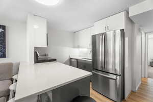 Kitchen with stainless steel appliances, white cabinets, light wood-style flooring, a kitchen bar, and a textured ceiling