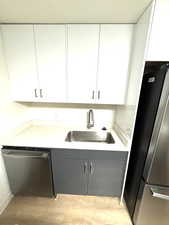Kitchen with white cabinets, stainless steel appliances, light wood-type flooring, and gray cabinetry