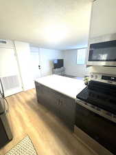 Kitchen with stainless steel appliances, a peninsula, light countertops, a textured ceiling, and light wood-style flooring