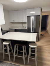 Kitchen with a breakfast bar, stainless steel appliances, a textured ceiling, light wood-style floors, and white cabinets