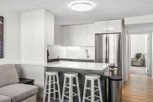 Kitchen with a peninsula, freestanding refrigerator, white cabinets, a textured ceiling, and light wood-style floors