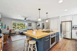 Kitchen with a kitchen bar, butcher block countertops, hanging light fixtures, stainless steel appliances, and white cabinets
