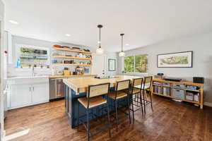 Kitchen featuring open shelves, a kitchen breakfast bar, pendant lighting, white cabinetry, and dishwasher