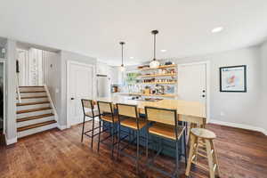 Kitchen with open shelves, hanging light fixtures, a center island, dark wood-type flooring, and a kitchen bar