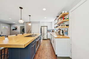 Kitchen featuring butcher block countertops, a breakfast bar area, open shelves, decorative light fixtures, and recessed lighting