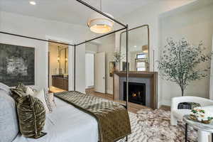 Bedroom with recessed lighting, ensuite bath, a warm lit fireplace, and wood finished floors