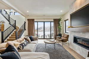 Living room with light wood finished floors, recessed lighting, a glass covered fireplace, and stairway