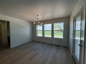 Unfurnished dining area featuring a textured ceiling, a chandelier, and dark wood finished floors